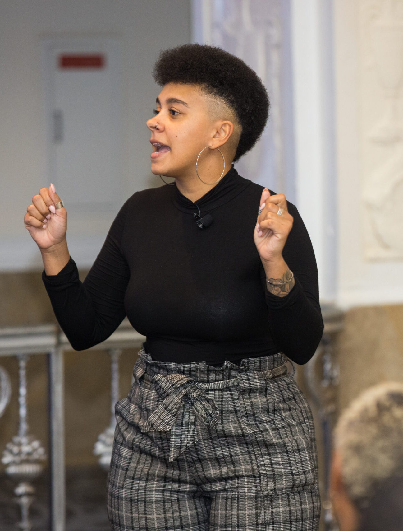 Christina performing a workshop at the National Association of Chapter 13 Trustees conference in 2024. She's holding her hands up in clenched fists for emphasis while wearing a black long sleeve shirt and grey plaid slacks.